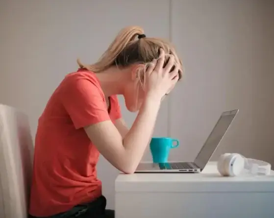 A woman at a desk holds her head in her hands in front of a laptop.