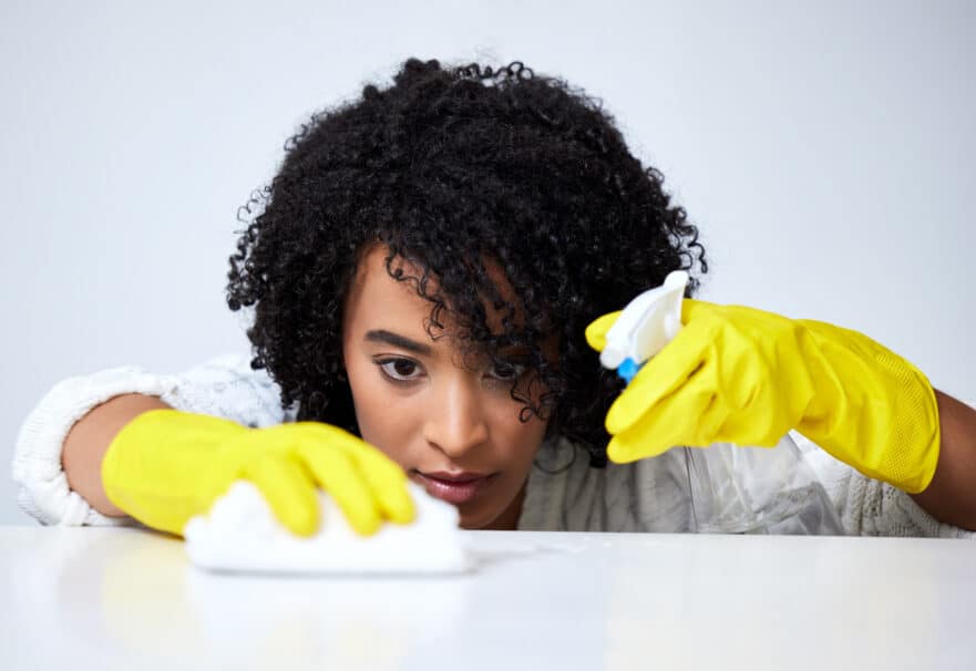 woman deep cleaning a counter with yellow gloves, a sponge, and a spray bottle