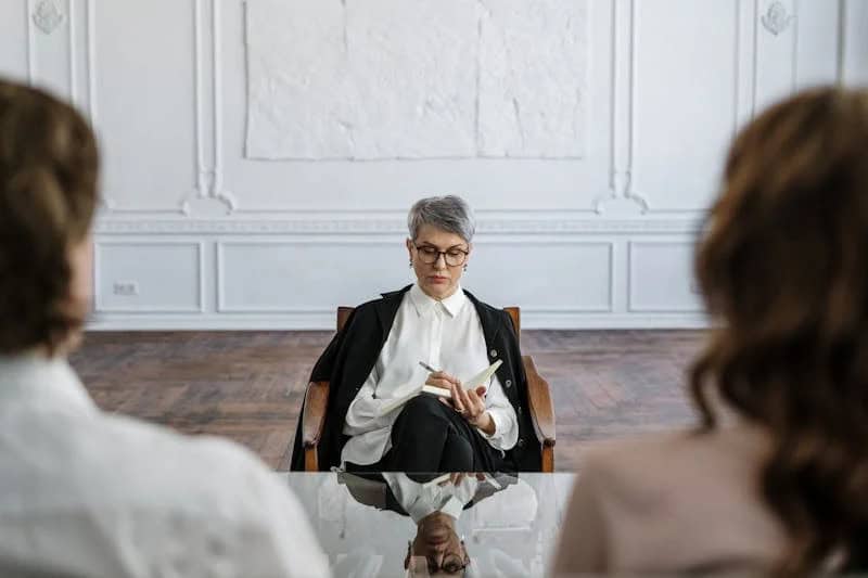 Older woman talking to 2 adults (a man and a woman) during a therapy session