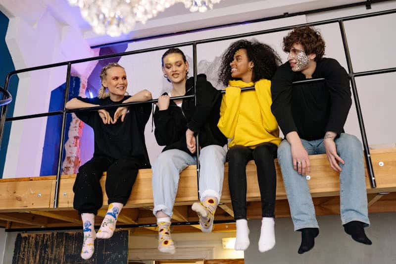 young adults sitting behind a railing with legs dangling and talking together