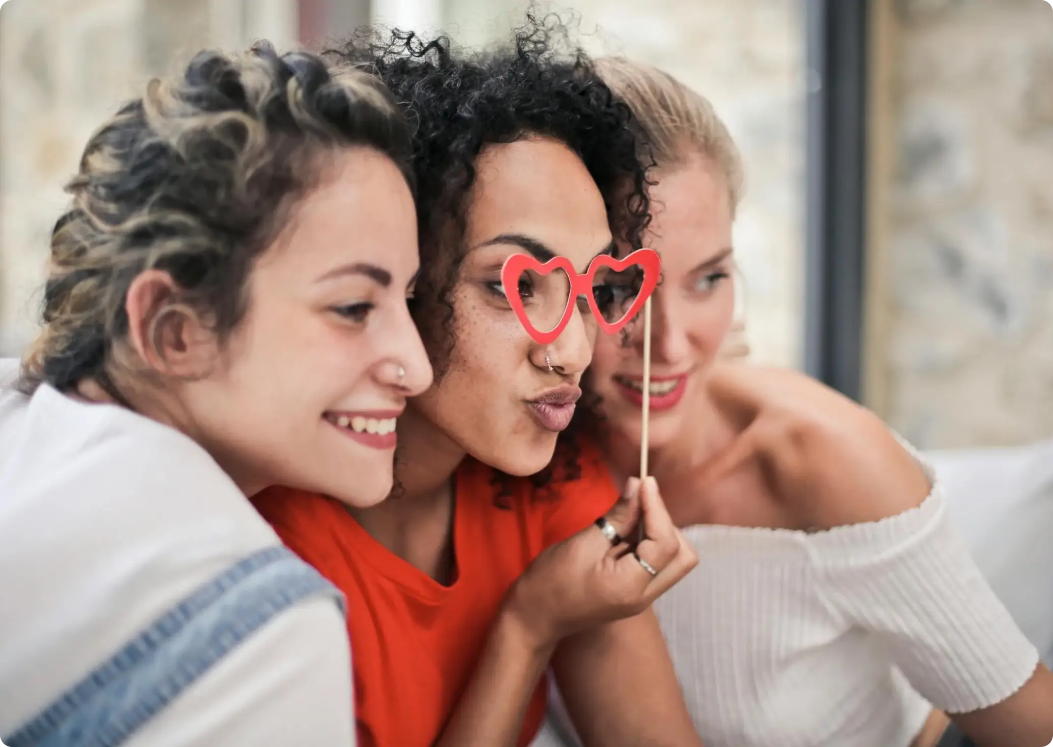 three ladies posing for a picture. the lady in the middle is holding a heart masquerade mask