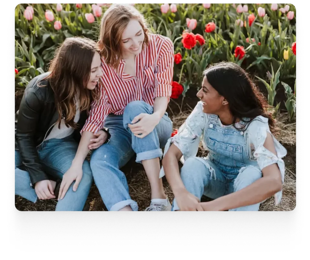 three ladies sitting on flower fields smiling and talking to each other