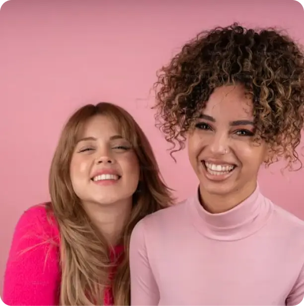 two ladies smiling with a pink background