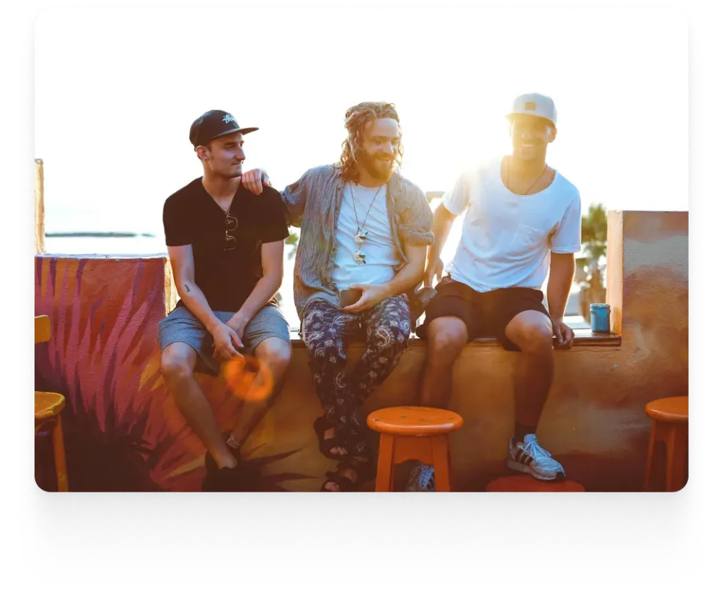 three guys sitting in a bench with the sunset on their background