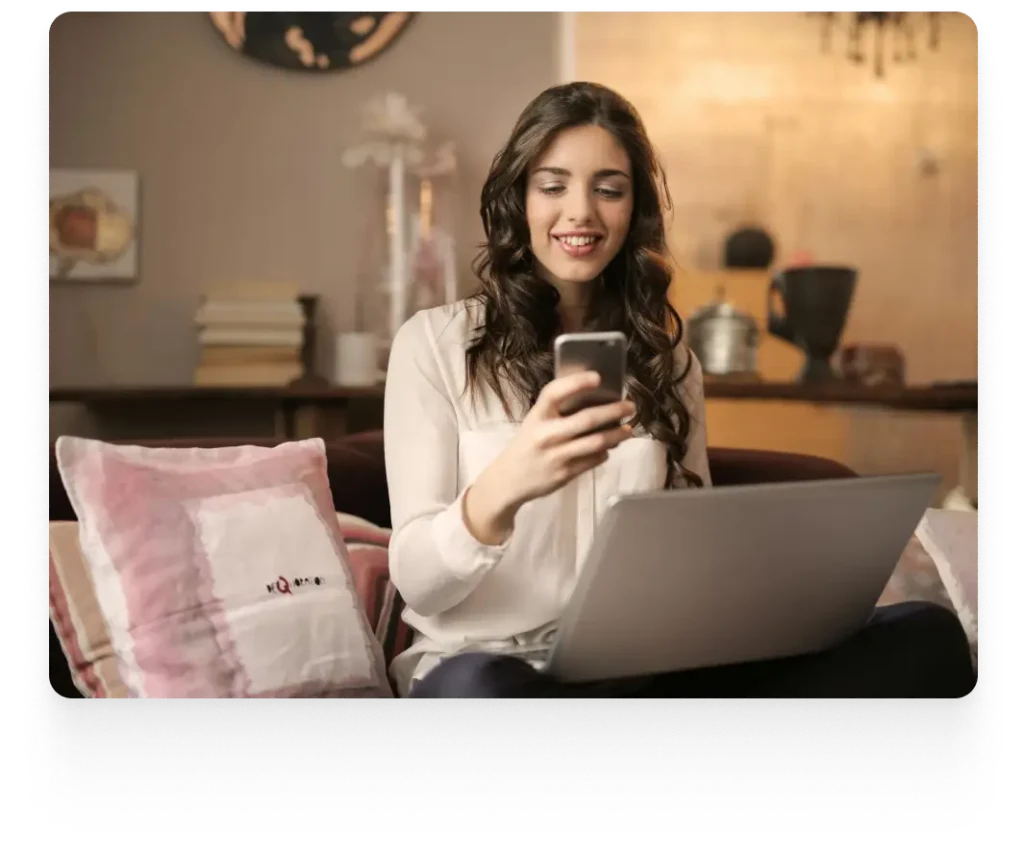 a lady smiling while reading something from her phone with a laptop on her lap