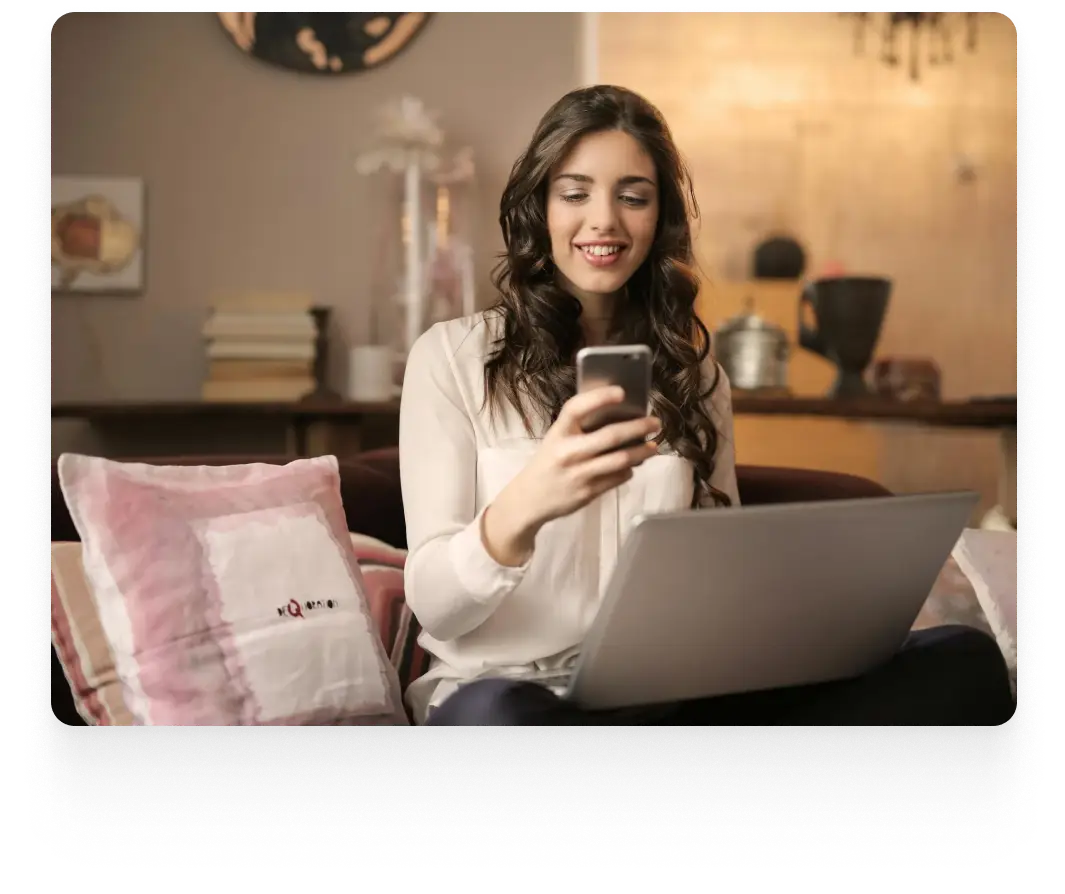 a lady smiling while reading something from her phone with a laptop on her lap