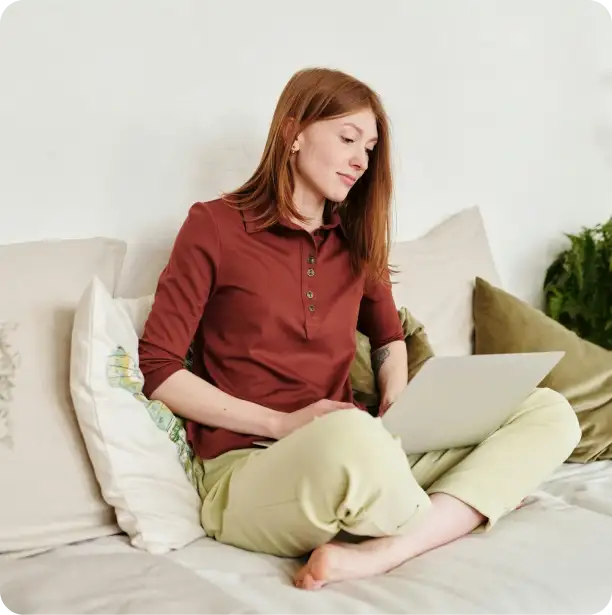 a woman sitting cross legged on a sofa while working on her laptop