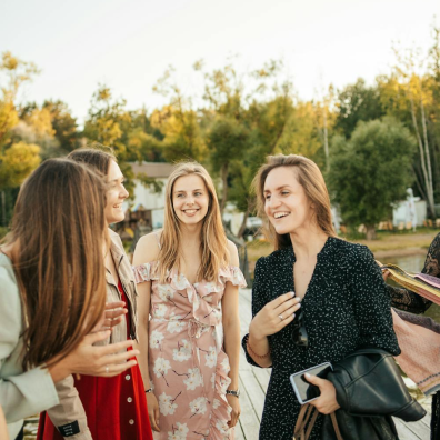 young adult women chatting and smiling together in from of a background of dense trees