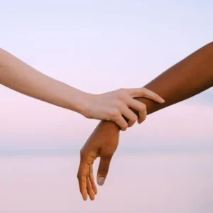 one dark skinned and one light skinned arm, one hand holding onto the wrist of the other arm amidst a peaceful sunrise background