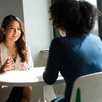 2 young adult women chatting across the table from one another