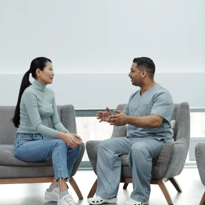 a man and a woman sit across from each other on a couch and a chair chatting amidst a gray background