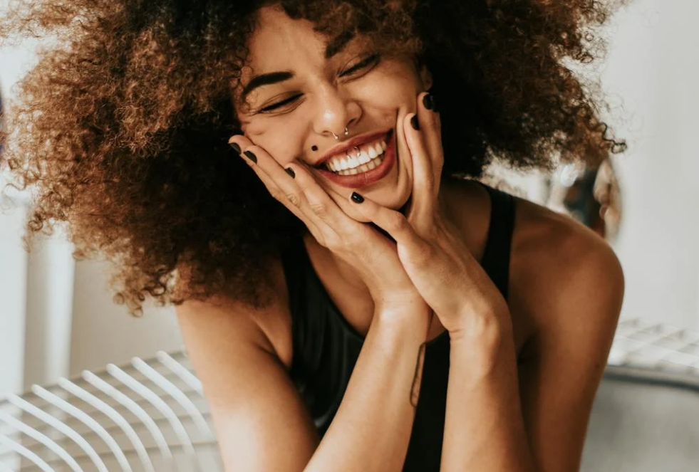 woman sitting and smiling with both hands resting on her cheeks