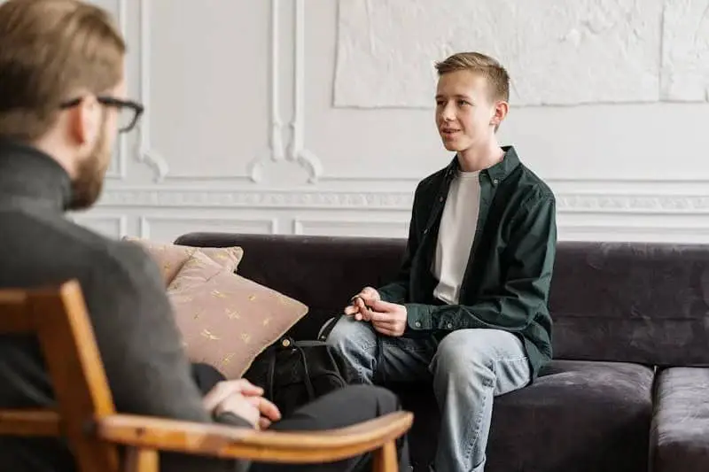 Young adult male sitting on the couch across from his therapist talking.