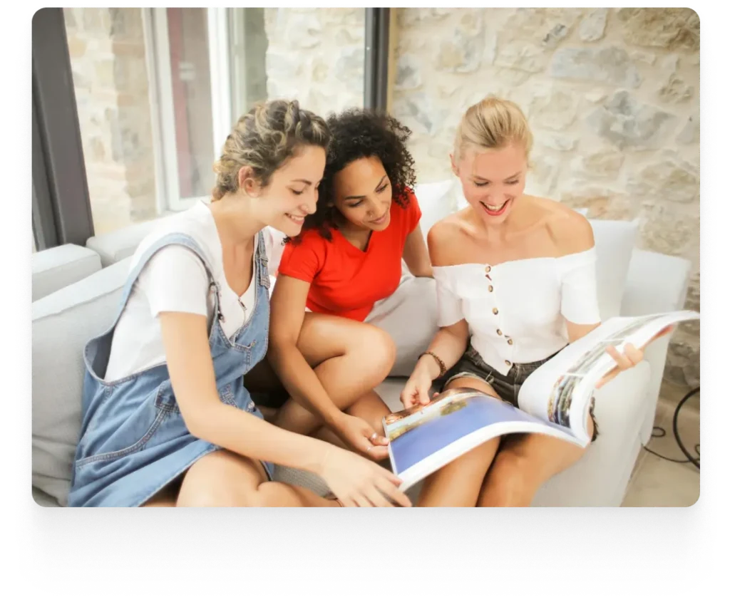 three ladies sitting on a sofa sharing a magazine