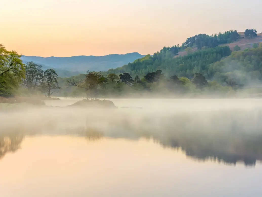 a picture of a mist filled lake with the mountains in the background